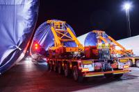 Two red clamp trailers with wind power tower sections loaded in them.