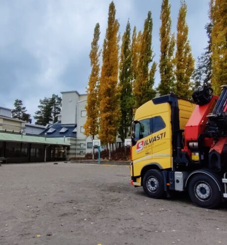 Yellow truck in front of a school on an autumn day.