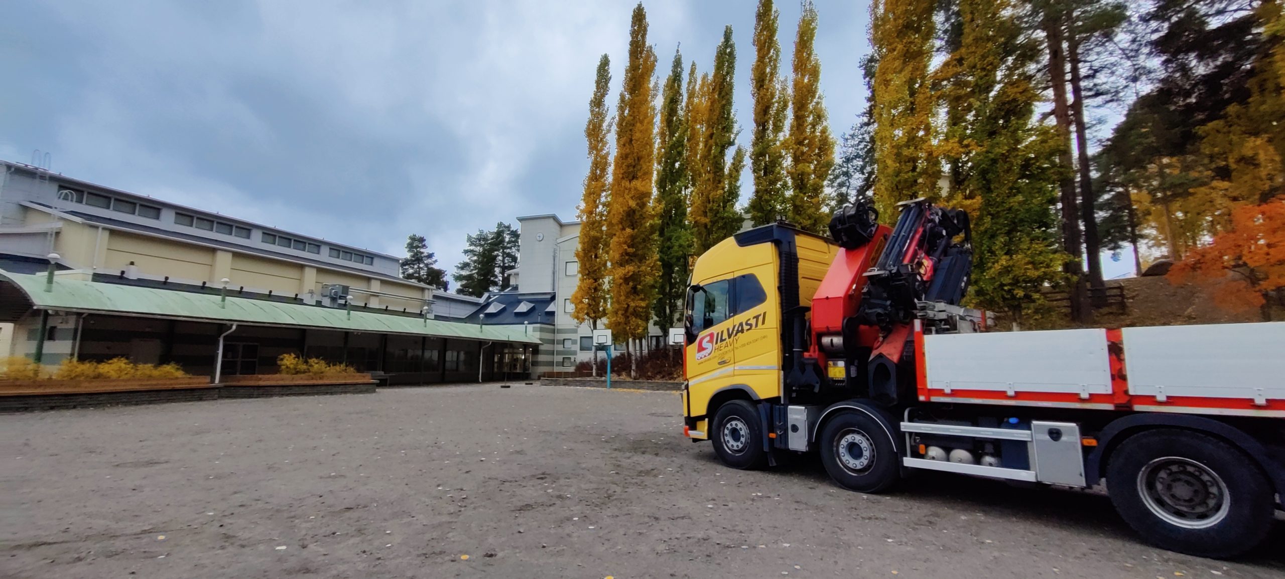 Yellow truck in front of a school on an autumn day.